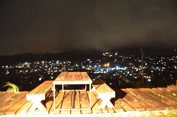 A wooden deck with a table and benches overlooking a cityscape at night.