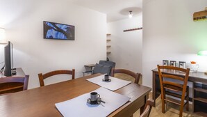 A dining area with a wooden table, chairs, a television mounted on the wall, and a ceiling light fixture. - GuestHost - Modern APT just 2 steps from the Ciclovia! x3 (Tarvisio)