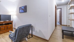A living room with a TV, a sofa, a wooden entertainment unit, and a hallway leading to a bathroom. - GuestHost - Modern APT just 2 steps from the Ciclovia! x3 (Tarvisio)