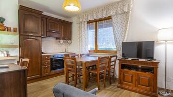 Una cucina compatta con mobili in legno, un tavolo da pranzo con sedie, una televisione e una finestra con tende.