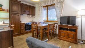 A compact kitchen with wooden cabinets, a dining table with chairs, a TV, and a window with curtains. - GuestHost - Modern APT just 2 steps from the Ciclovia! x3 (Tarvisio)