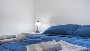 Un letto rifatto con lenzuola blu, una lampada sul comodino e asciugamani piegati.