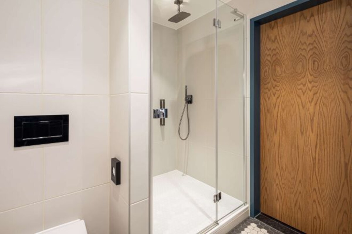 A modern bathroom with a glass shower enclosure, a wooden panel wall, and a white tiled floor.