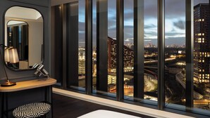 Habitación de hotel moderna con un amplio ventanal que ofrece vistas a la ciudad al anochecer.