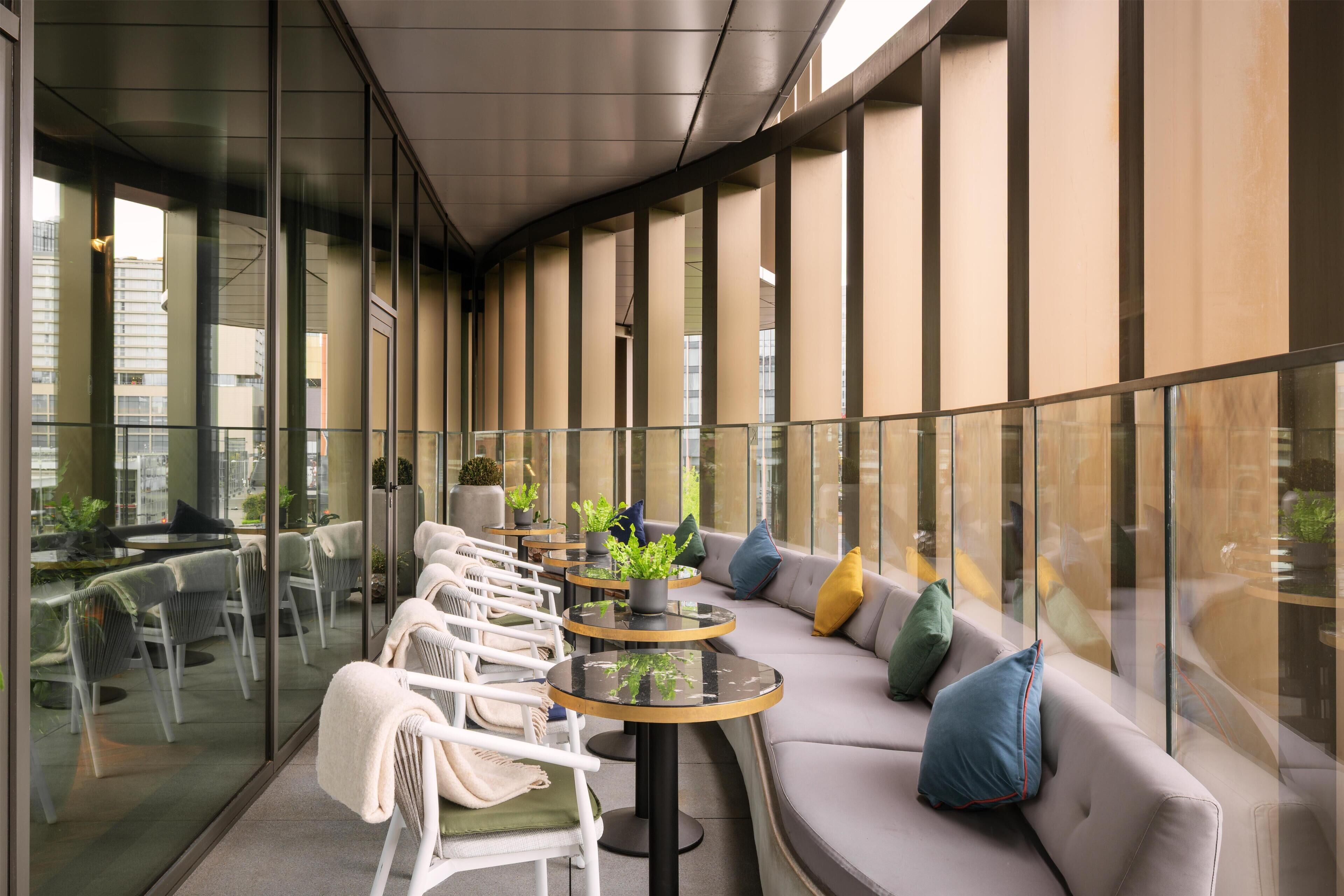 A modern indoor space with a glass railing, seating area, and potted plants.