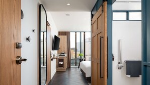 Una habitaci ón de hotel con una cama grande, un escritorio con televisión, un baño con ducha y vistas de la ciudad a través de amplios ventanales.