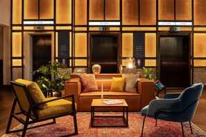 A lobby with a sofa, chairs, a coffee table, and two elevators. - The Gantry London, Curio Collection by Hilton (London)