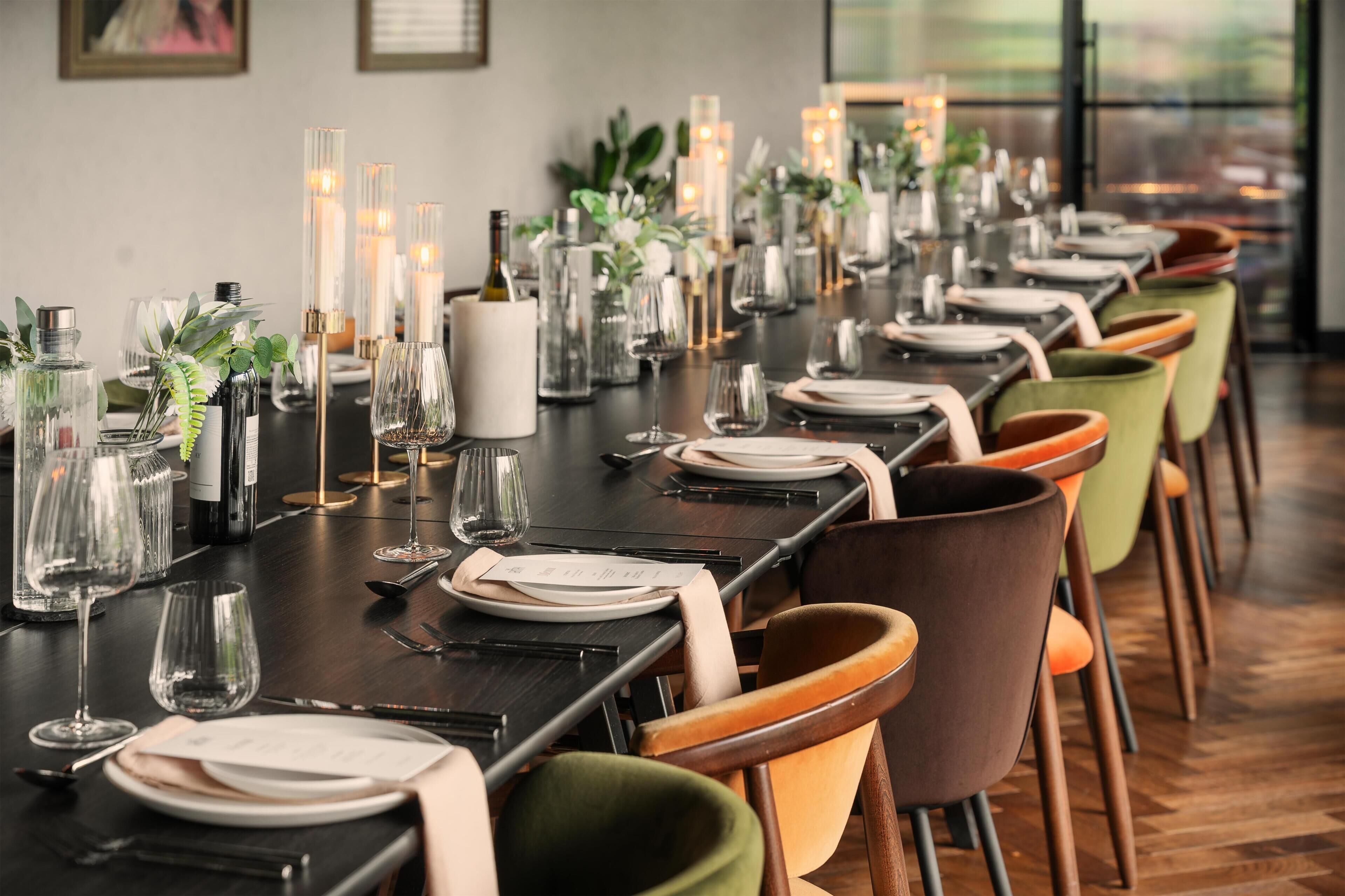 A long dining table set with chairs, candles, and glassware.