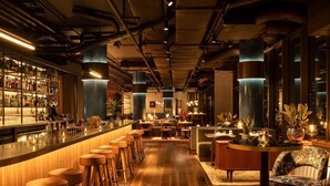 Una zona de bar con taburetes, barra y un área de estar con mesas y sillas.