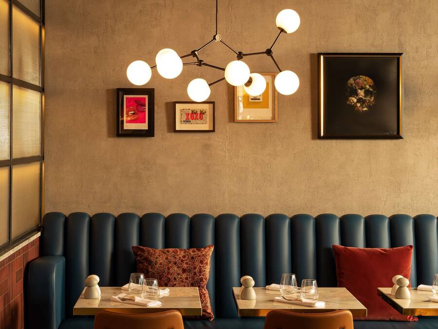 A restaurant with a blue booth seating area, two tables with chairs, and a chandelier with multiple lights.