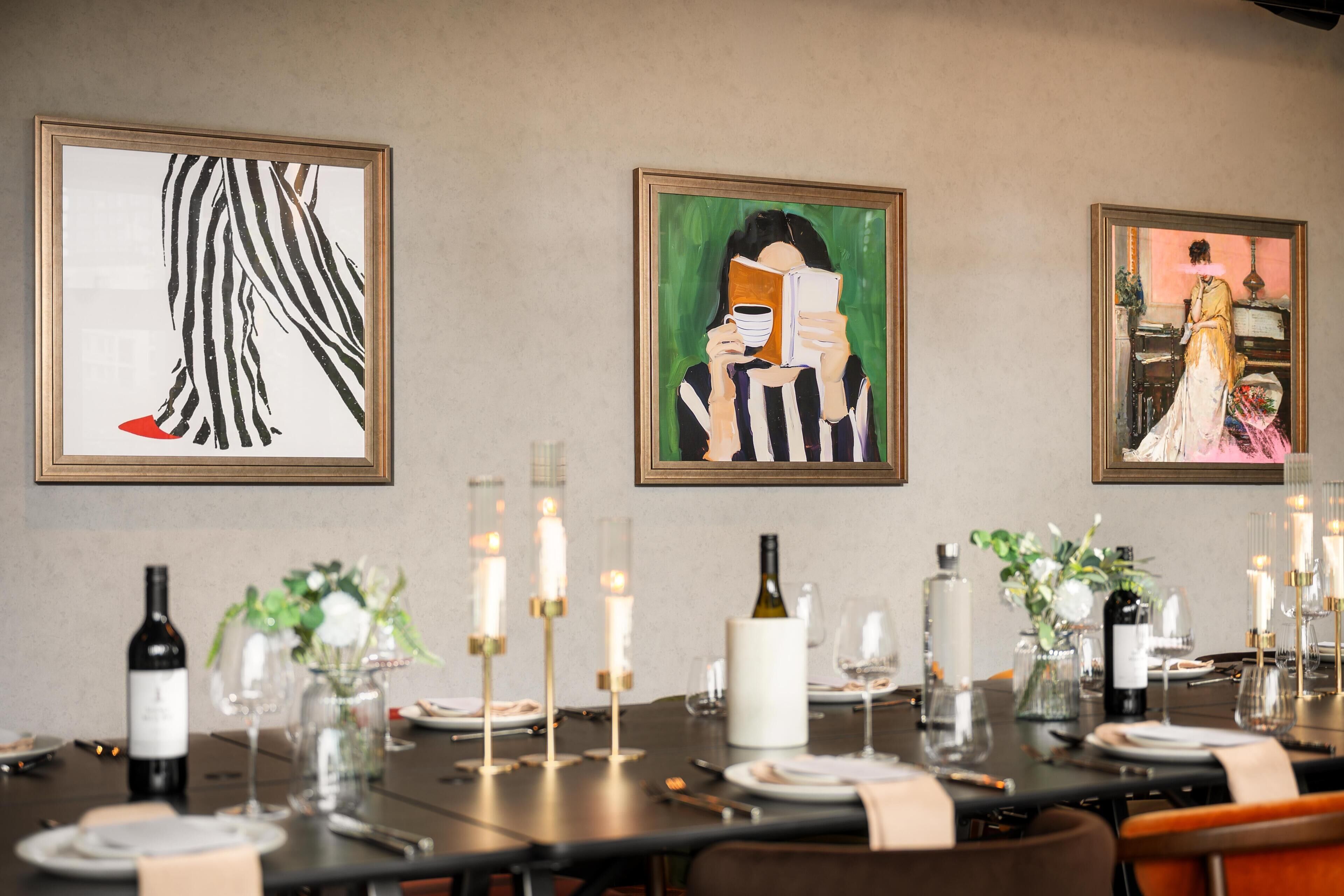 A dining area with a table set for four, framed artwork on the wall, and candles on the table.