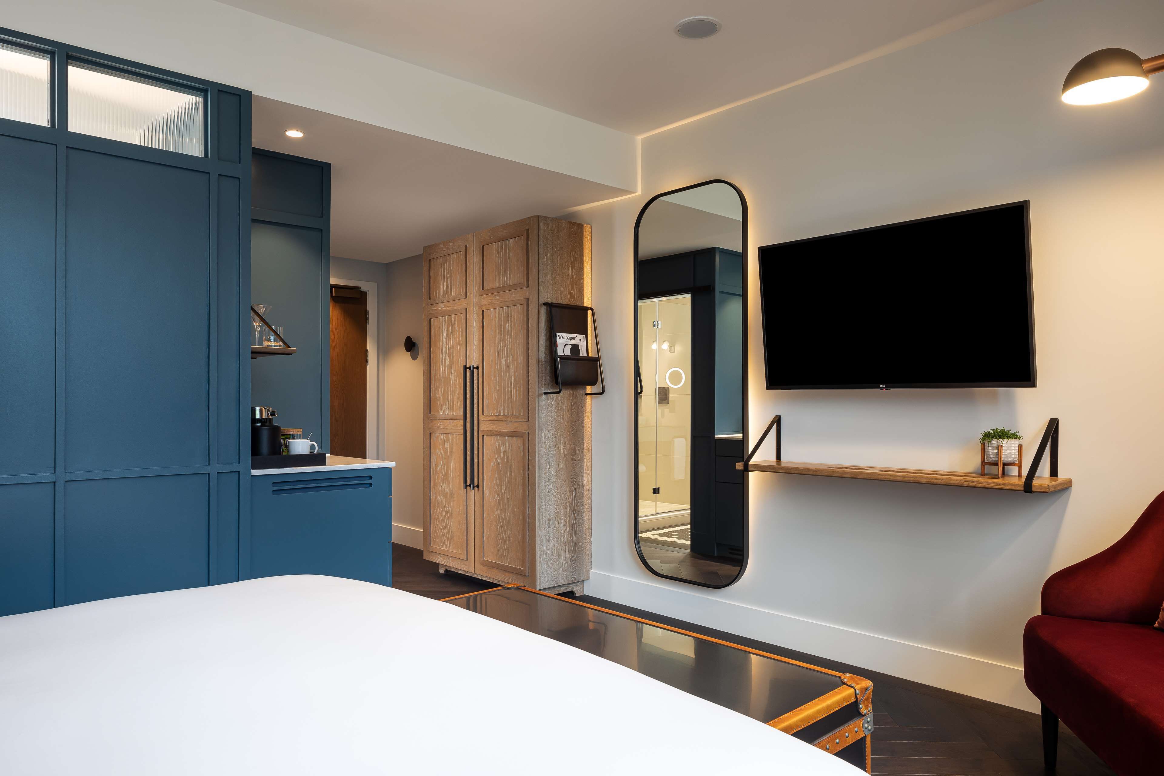 Een moderne slaapkamer met een groot bed, een kledingkast, een spiegel, een televisie en een rode stoel.