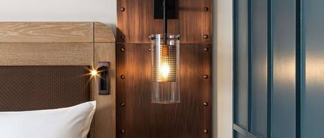 Ein ordentlich bezogenes Bett mit einem hölzernen Kopfteil, ein Nachttisch mit einer Lampe und eine blaue Wandverkleidung.