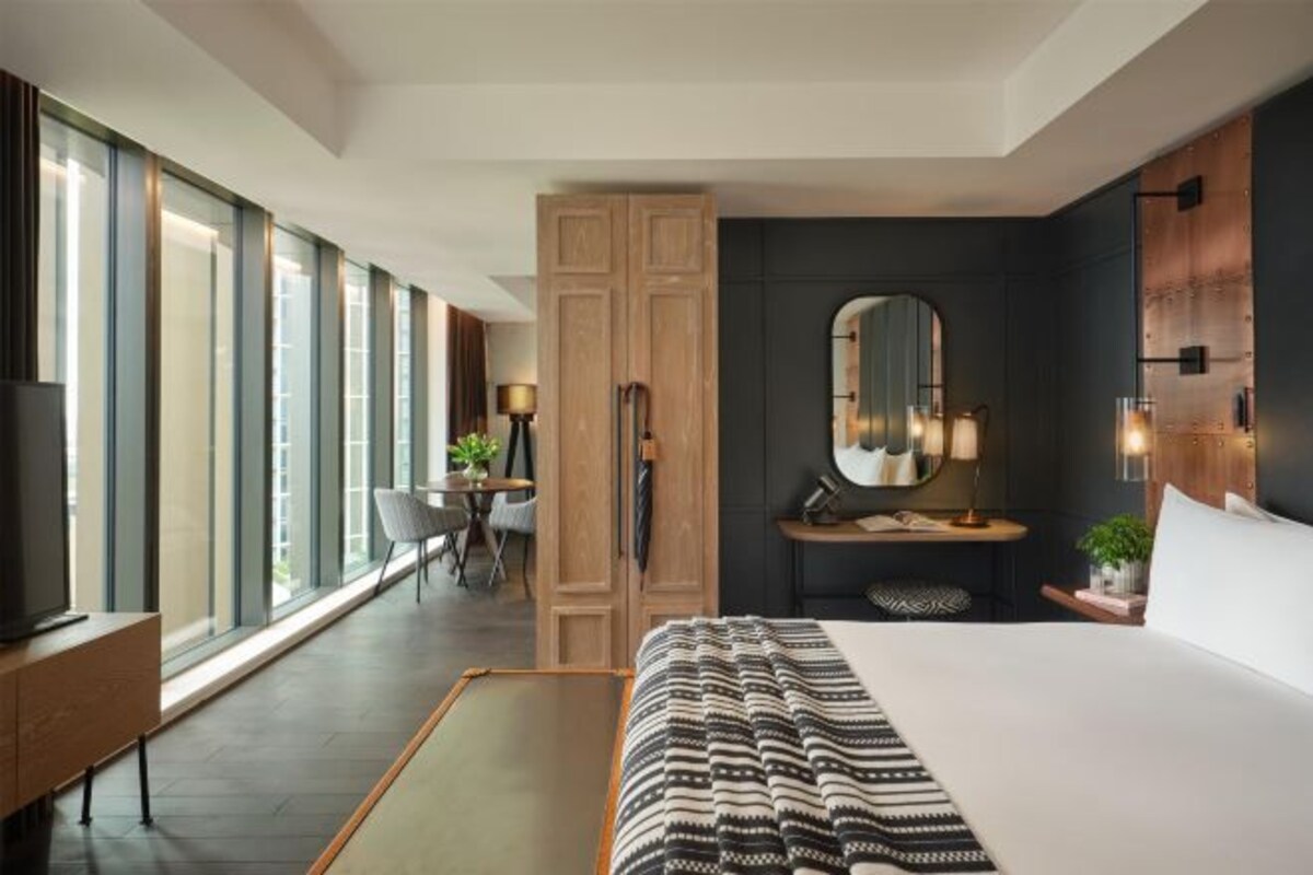 A modern hotel room with a large bed, a desk, a wardrobe, and a large window offering a view.