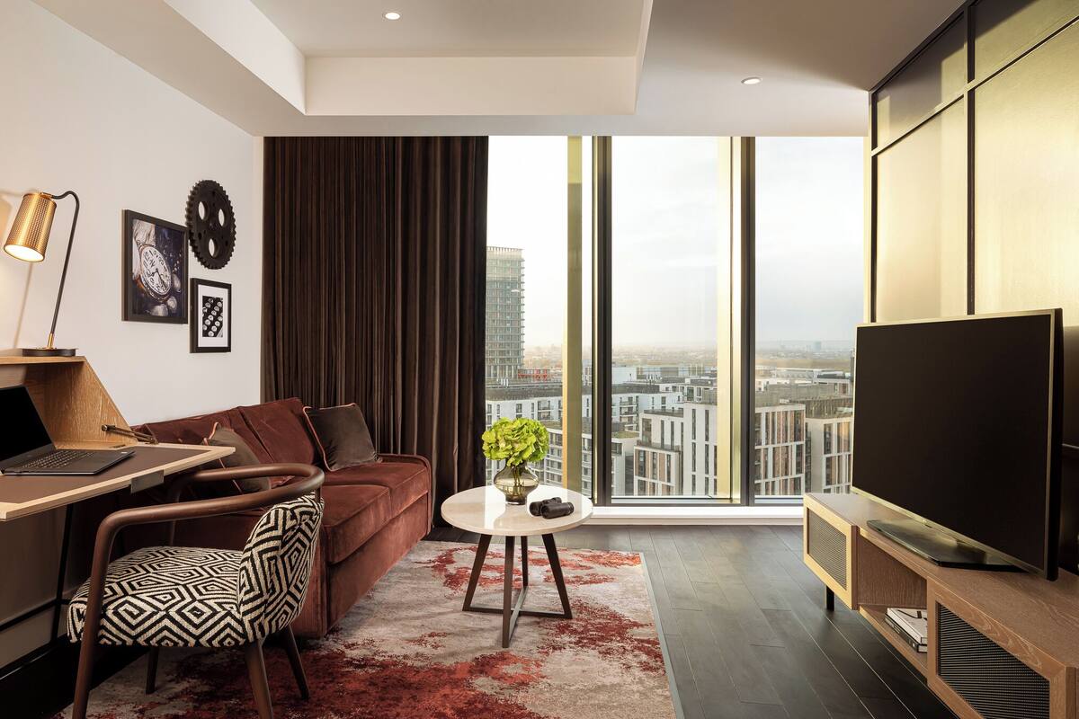A modern living room with a sofa, a coffee table, a TV, and a large window with a city view.