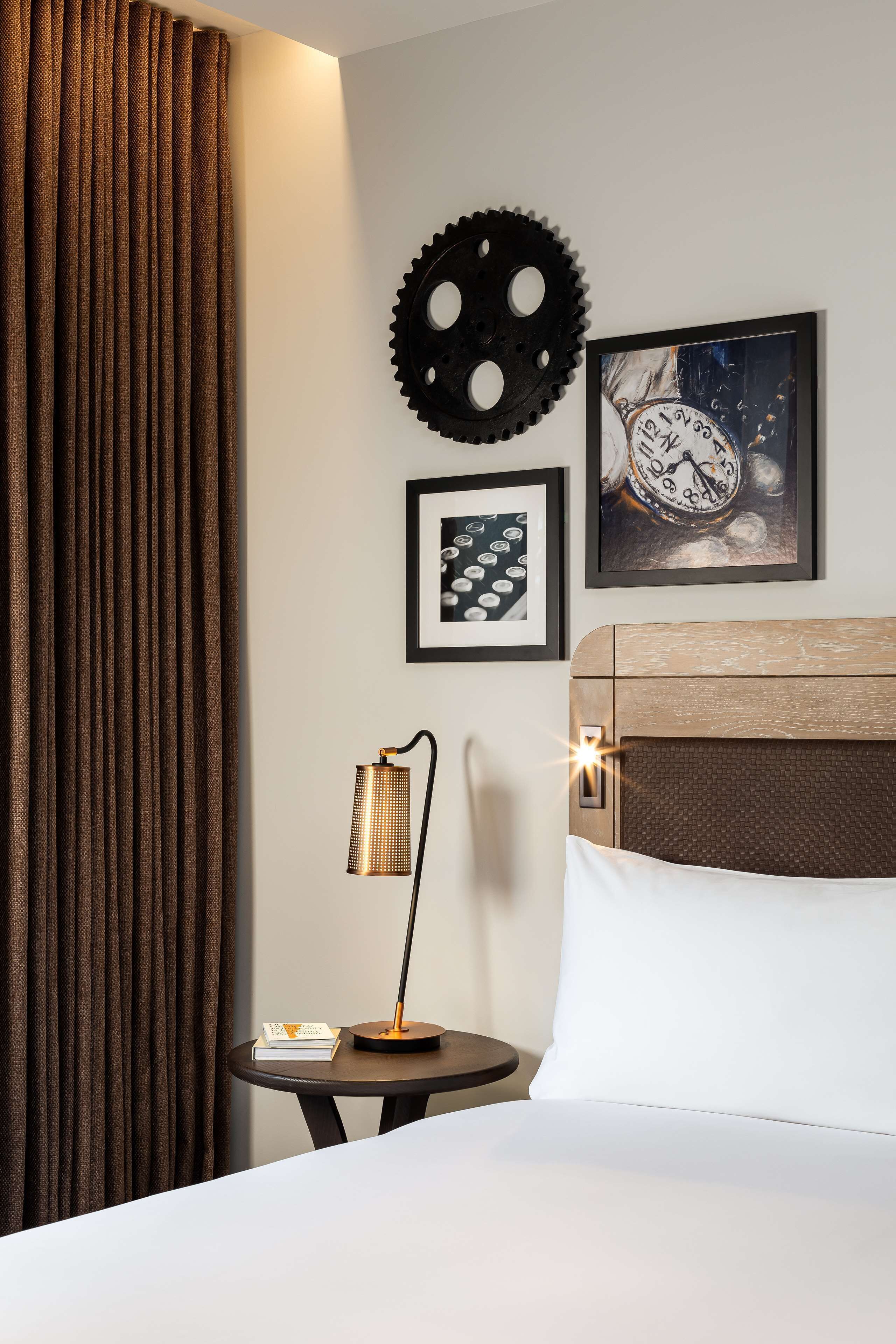 Une chambre d’hôtel avec un lit, une table de chevet avec une lampe, une horloge et une décoration en forme d’engrenage au mur.