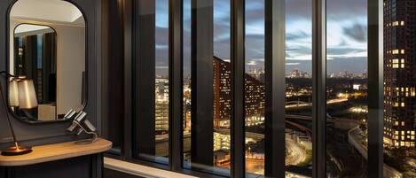 Habitación de hotel moderna con un amplio ventanal que ofrece vistas a la ciudad al atardecer.