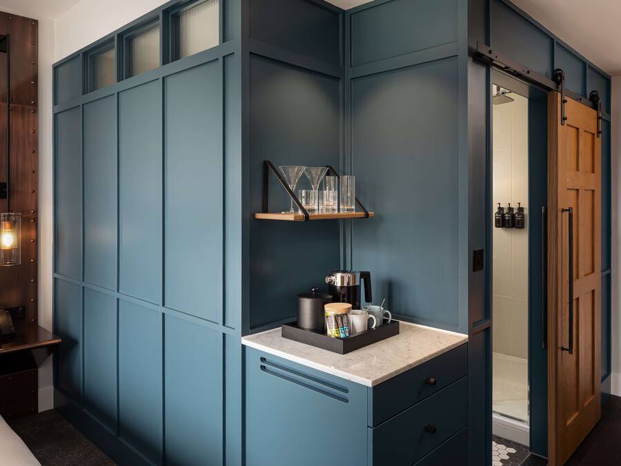 A modern bathroom with a blue vanity, a shower area, and a wooden door.