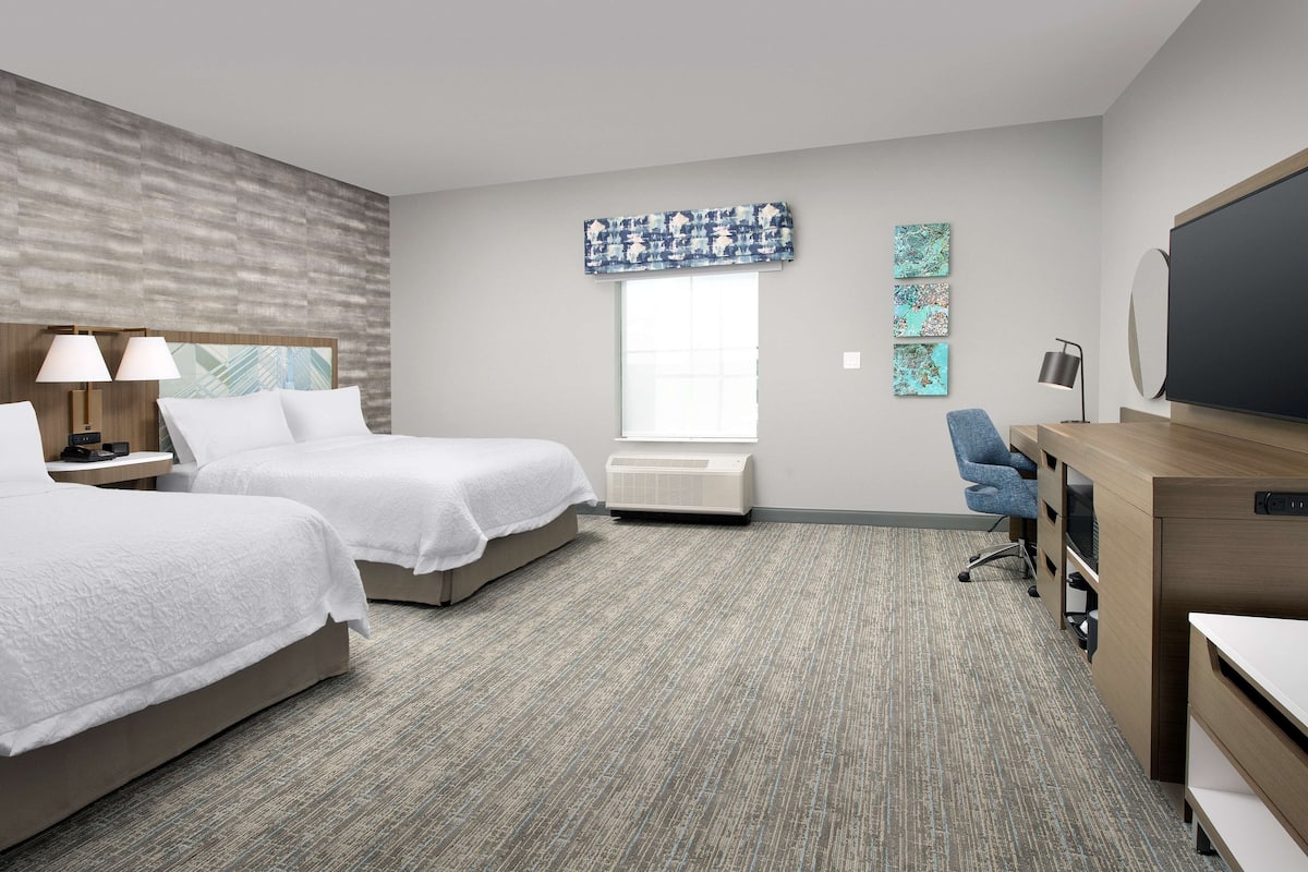 A hotel room with two beds, a desk, a chair, a large window with a view, and a flat-screen TV.