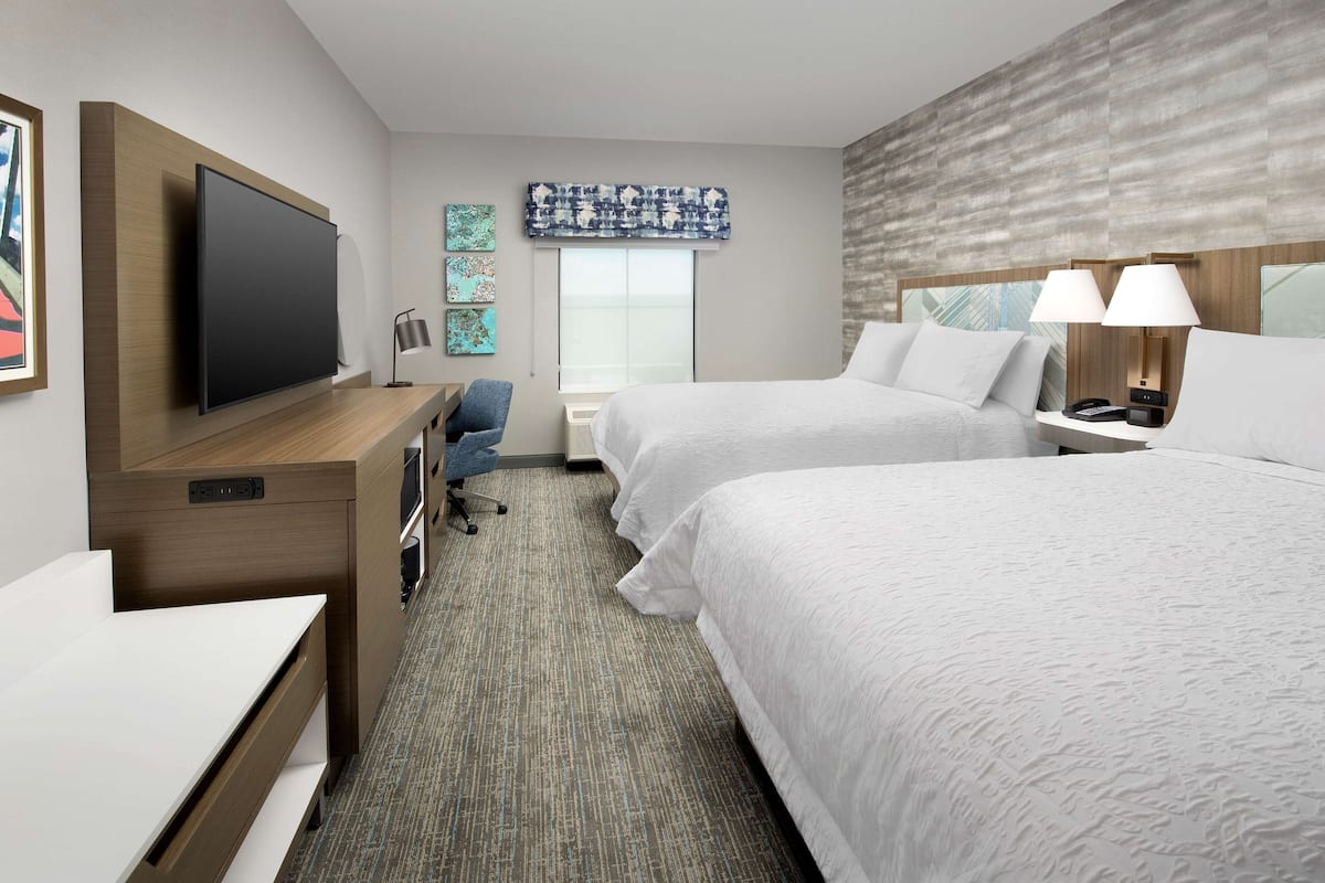 A hotel room with two beds, a desk with a TV, a chair, and a window with a view.