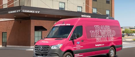 Una camioneta rosa de Hampton Inn estacionada frente a un edificio con un letrero que indica una altura libre de 3.6 metros.