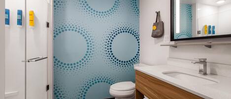 Une salle de bain moderne avec un mur à motifs bleus, des toilettes blanches, un meuble-lavabo en bois et un miroir au-dessus du lavabo.