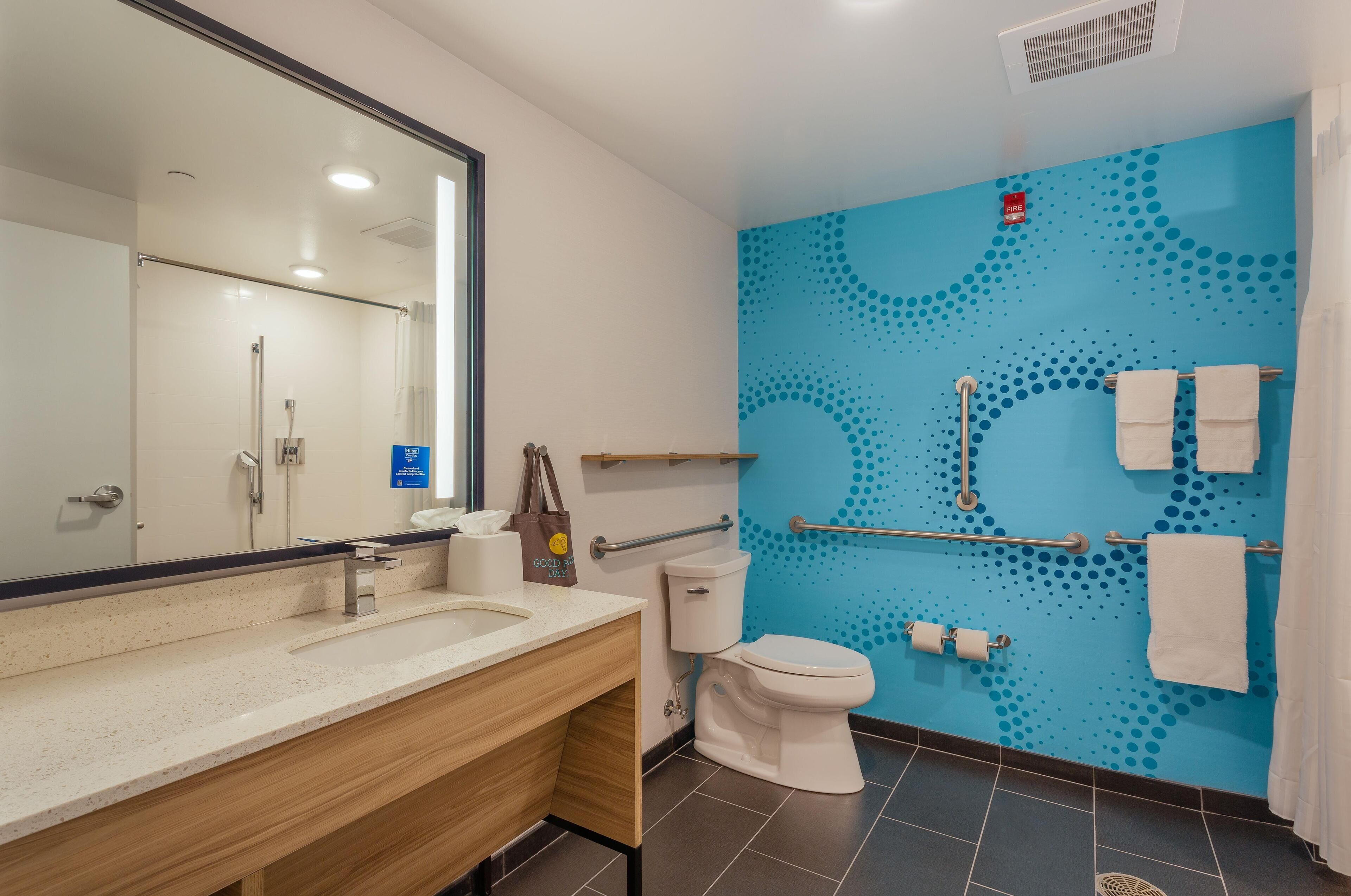 A modern bathroom with a blue wall, a white toilet, a sink with a mirror, and a towel rack.