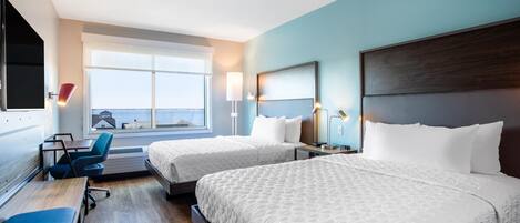 A hotel room with two beds, a desk, a chair, a TV, and a large window.