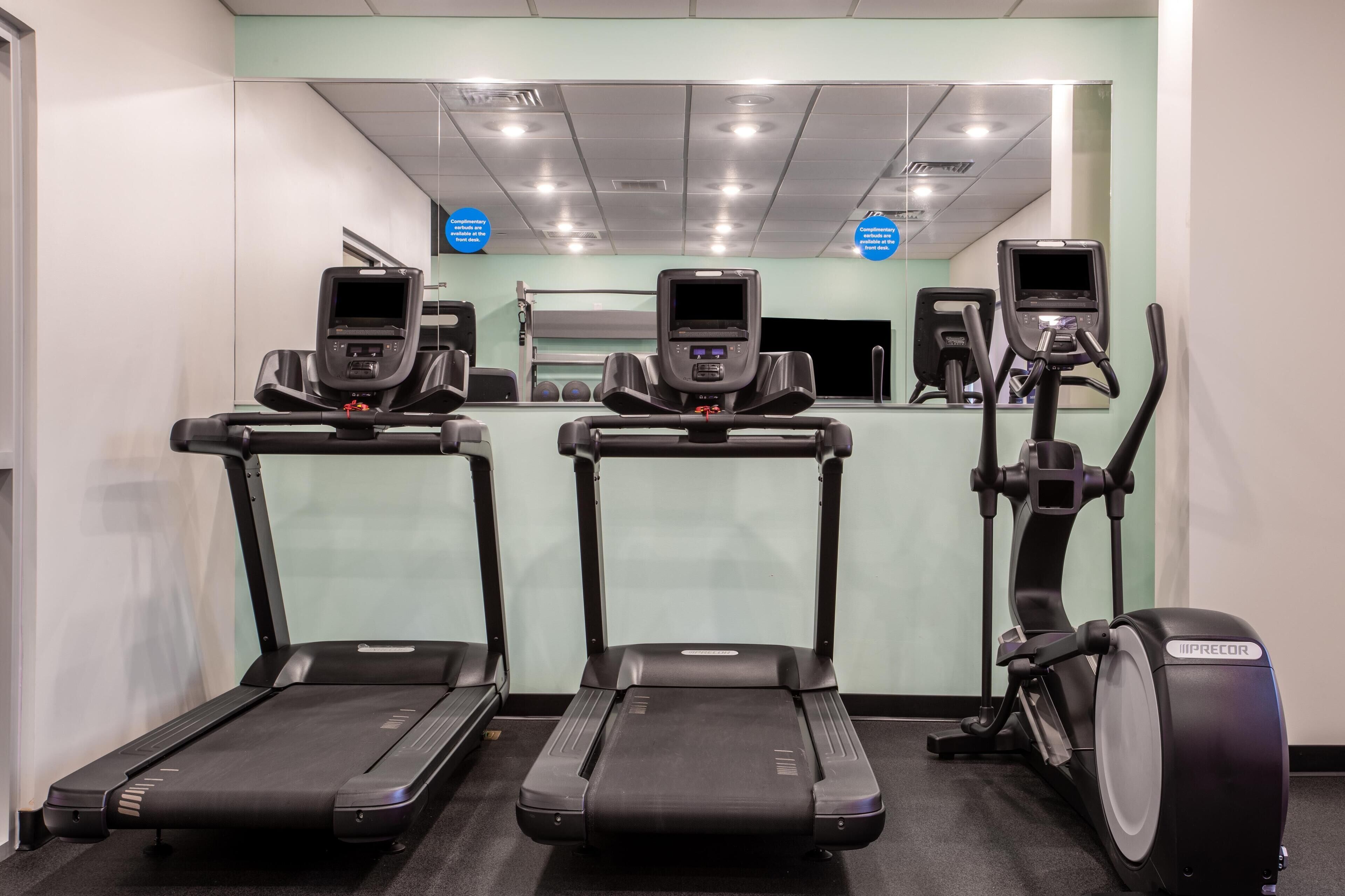 Trois appareils d’exercice dans une salle de sport, avec un mur et un plafond recouverts de miroirs et dotés d’un éclairage au plafond.