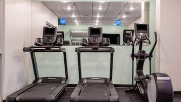 Three exercise machines in a gym with a mirrored wall and ceiling lights.