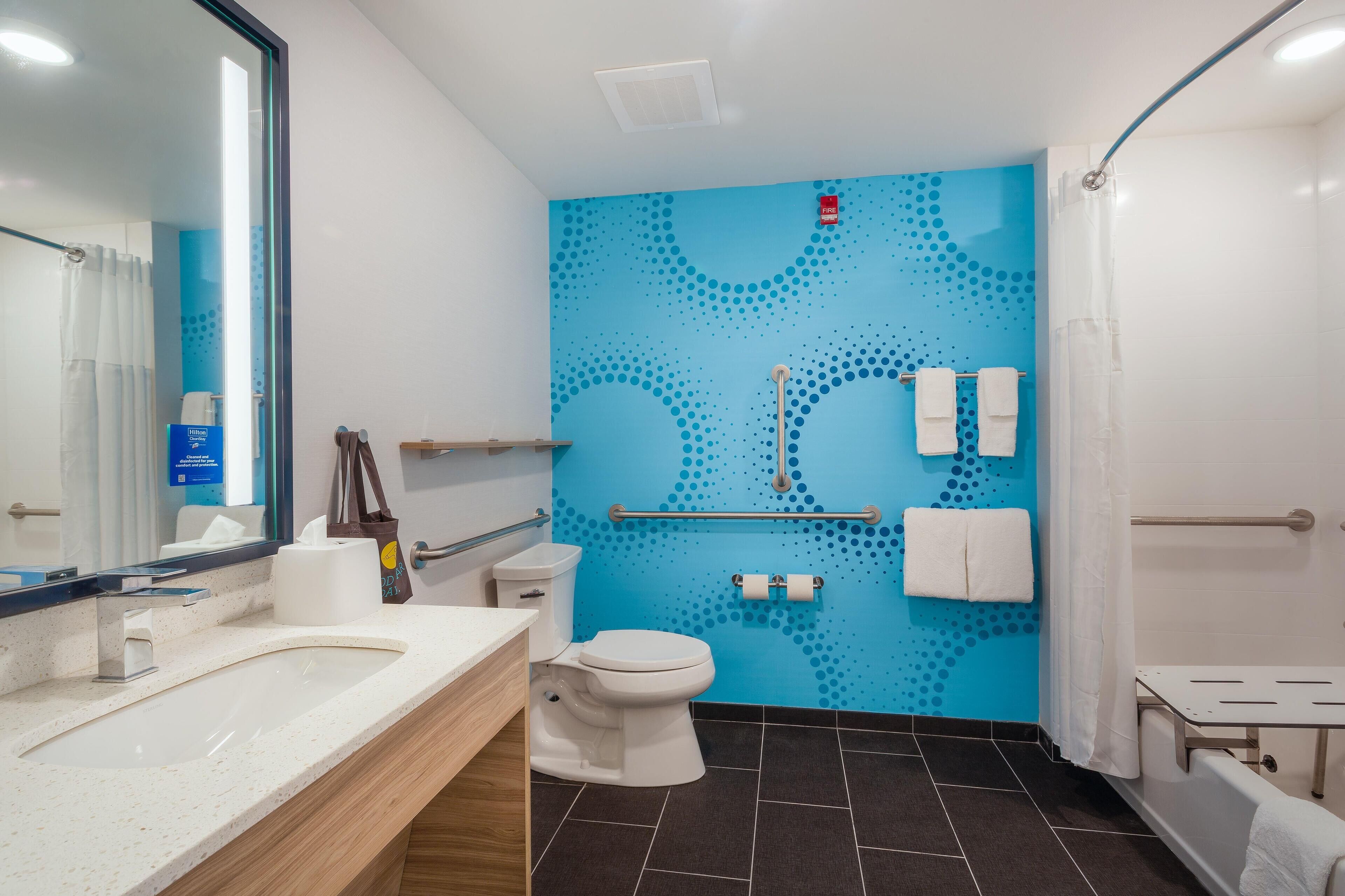 A modern bathroom with a blue patterned wall, a white toilet, a sink with a countertop, and a shower area.
