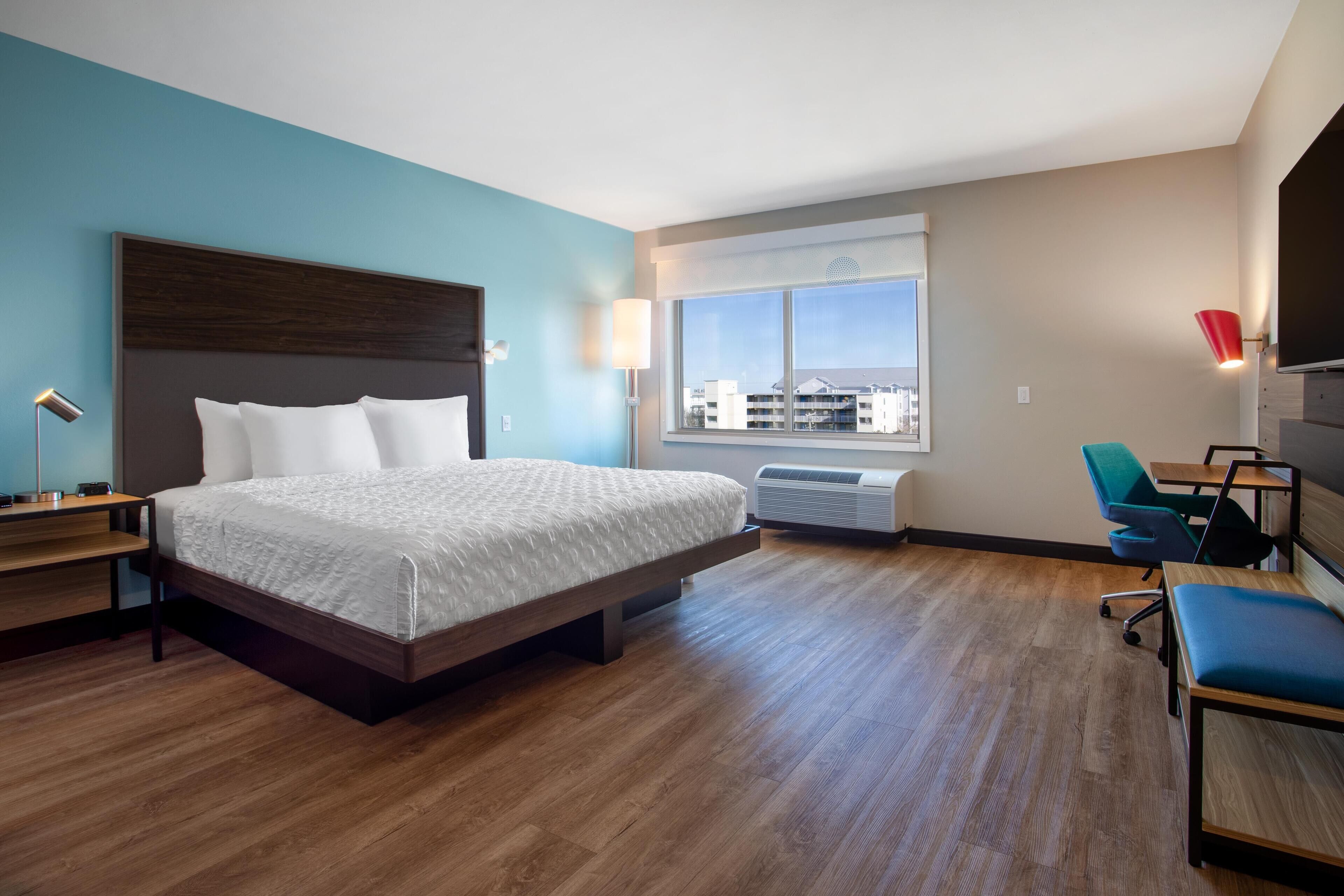 Habitación de hotel con una cama grande, un escritorio, una silla, un ventanal con vistas y un equipo de aire acondicionado.