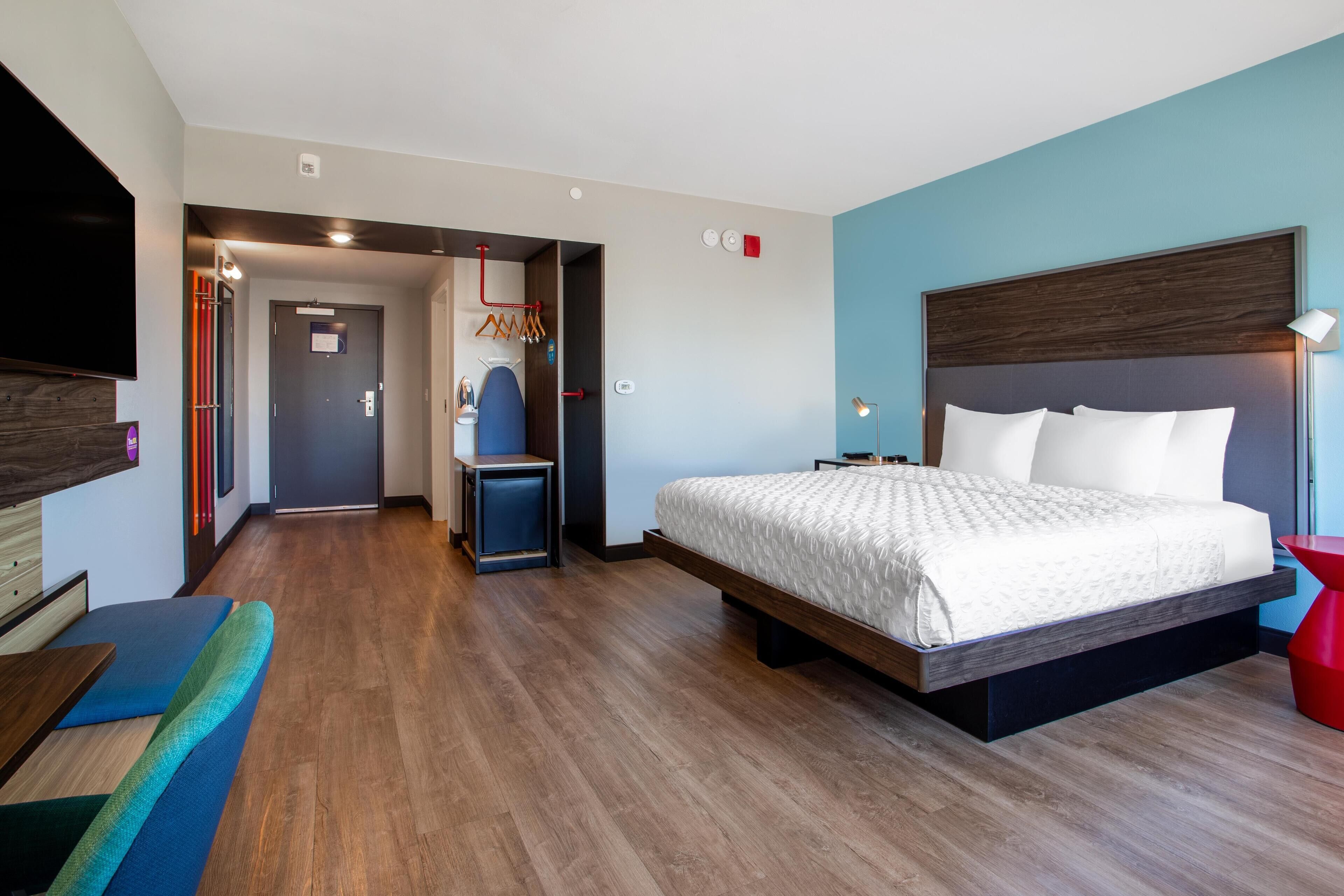 Una camera d'albergo moderna con un letto grande, una TV, un angolo salotto e un corridoio che porta al bagno.