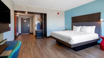 Ein modernes Hotelzimmer mit einem großen Bett, einem Fernseher, einer Sitzecke und einem Flur, der zu einem Badezimmer führt.