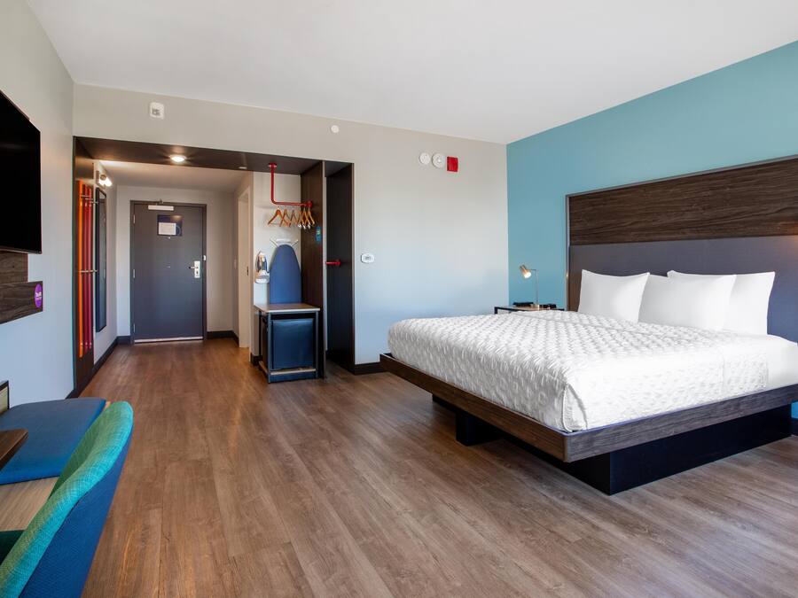 Ein modernes Hotelzimmer mit einem großen Bett, einem Fernseher, einer Sitzecke und einem Flur, der zu einem Badezimmer führt.