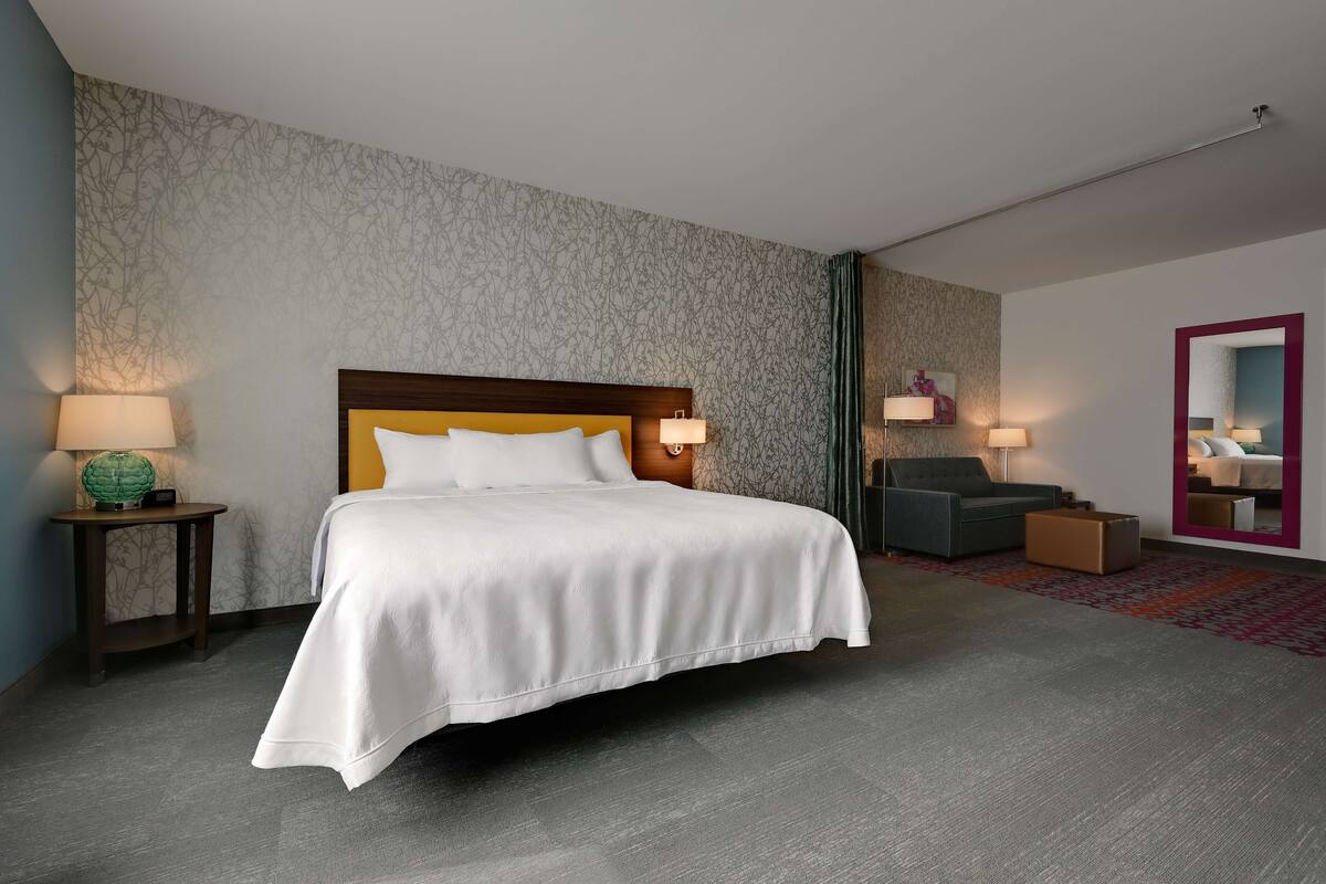 Una habitación de hotel con una cama grande, dos mesitas de noche con lámparas, un sofá y un espejo.
