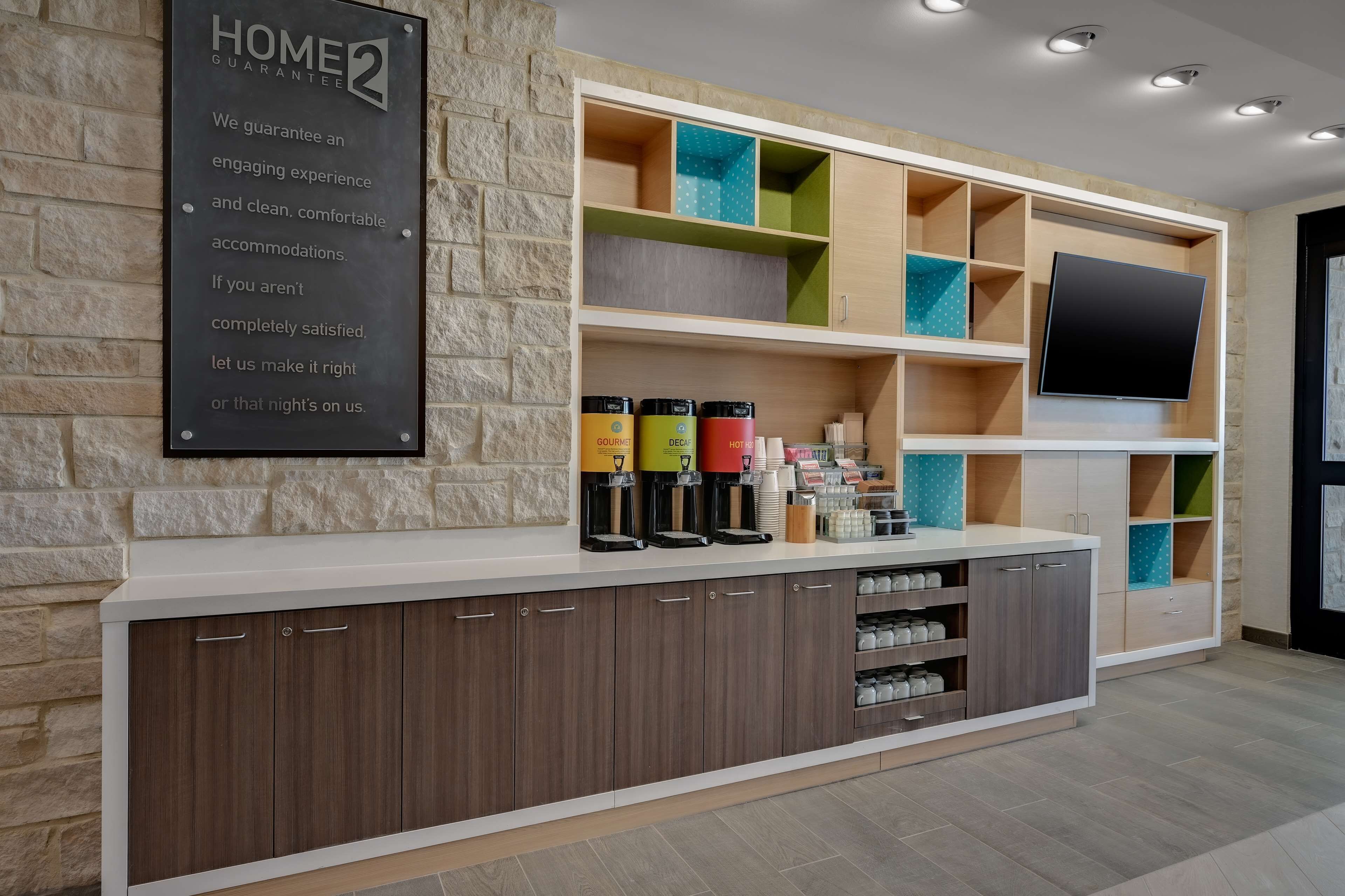 A reception area with a stone wall, a signboard, a counter with coffee dispensers, and a TV mounted on the wall.