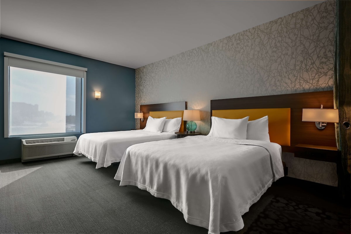 Habitación de hotel con dos camas, un ventanal grande y un papel tapiz estampado.