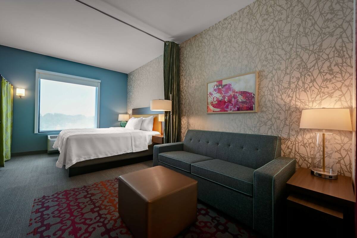 Habitación de hotel con cama, sofá, mesita y ventana con cortinas.