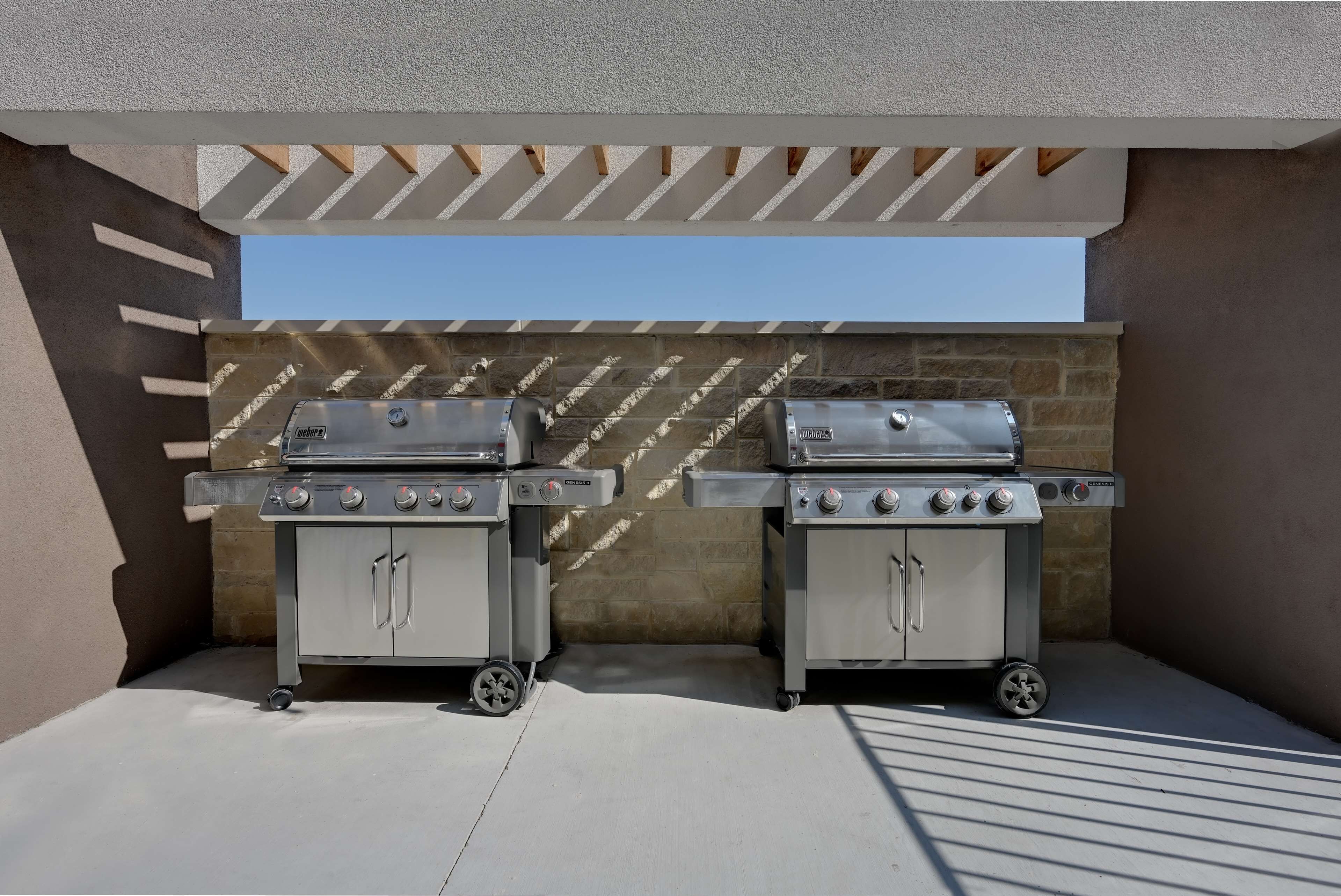 Twee draagbare gasgrills staan onder een pergola op een terras op het dak, met een stenen muur op de achtergrond.