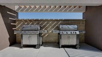 Twee draagbare gasgrills staan onder een pergola op een terras op het dak, met een stenen muur op de achtergrond.
