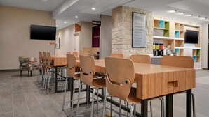 A modern conference room with a long wooden table and chairs, a stone accent wall, a television, and a colorful storage unit. - Home2 Suites by Hilton Temple Medical Center (Temple)