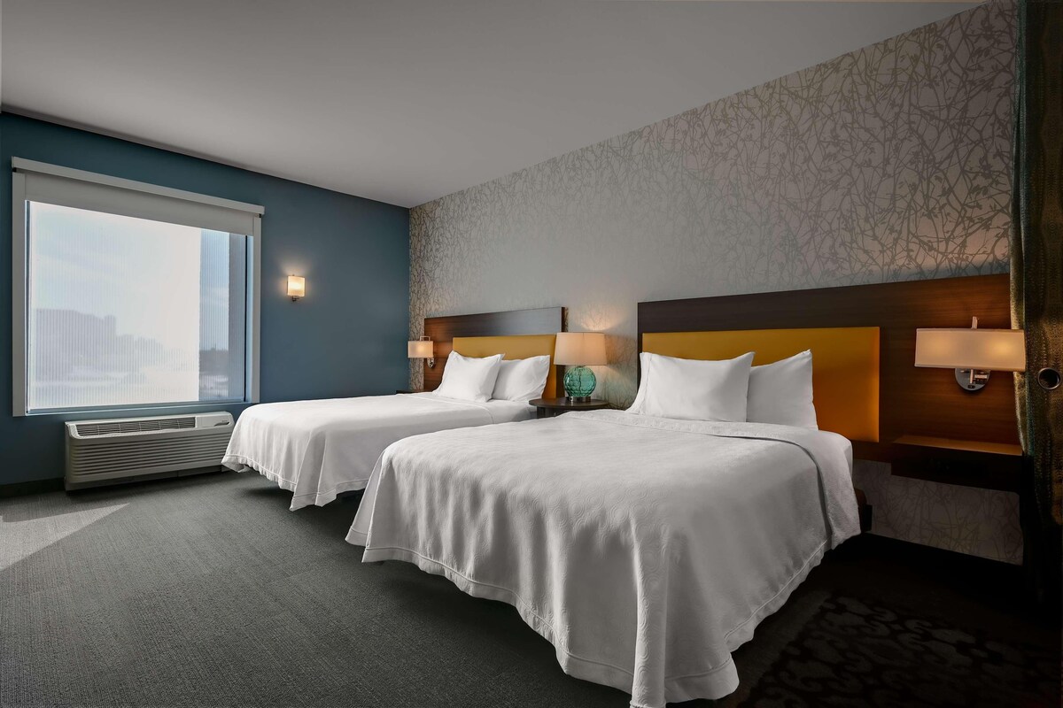 A hotel room with two beds, a large window, and a patterned wall.