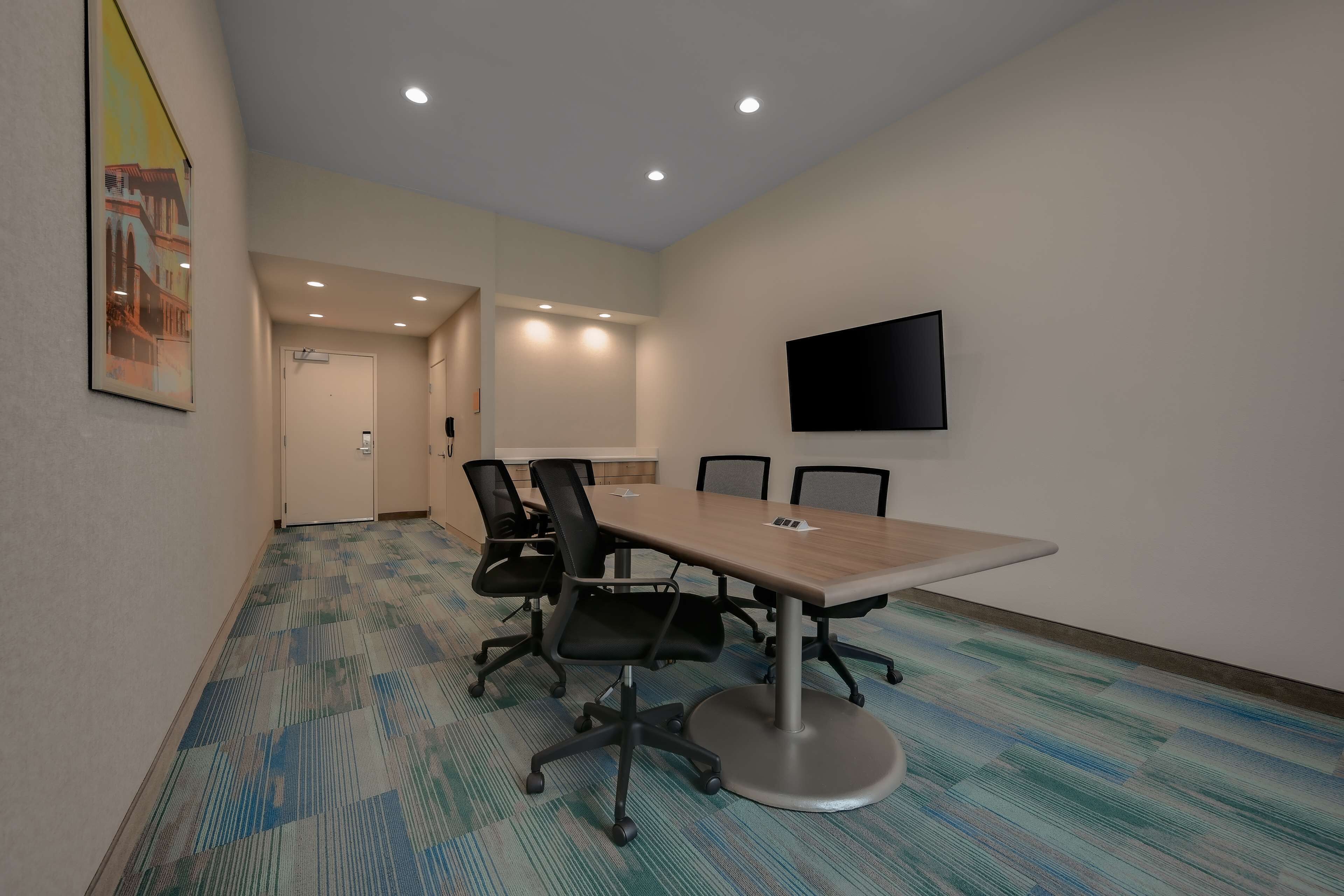 Une salle de conférence dotée d’une grande table, de chaises de bureau noires, d’un téléviseur fixé au mur et d’un tapis à motifs.