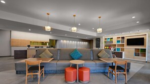 A modern living area with a sofa, two wooden chairs, a small round table, and a TV mounted on the wall. - Home2 Suites by Hilton Temple Medical Center (Temple)