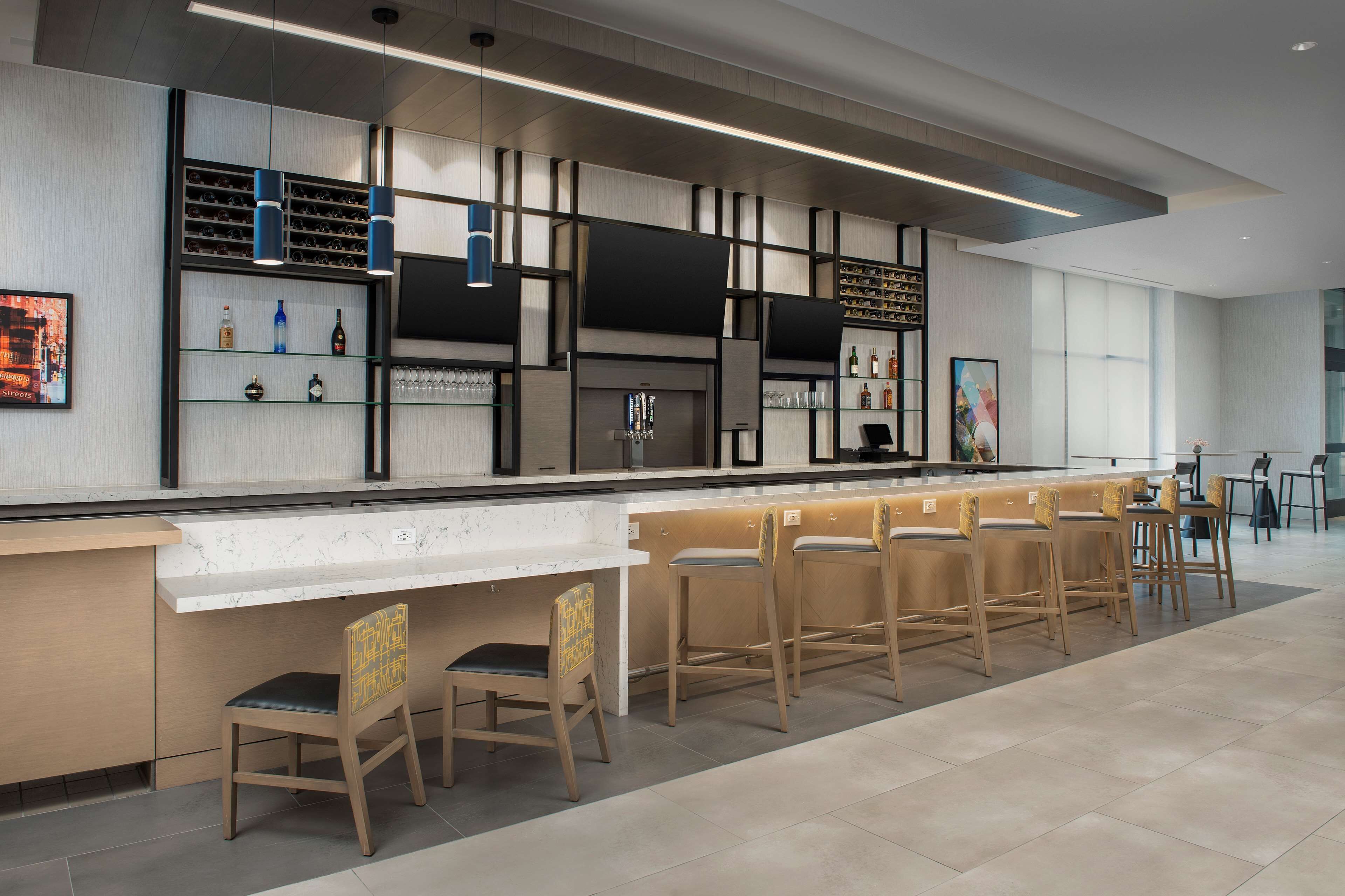 Un espace bar moderne doté d’un long comptoir, de plusieurs étagères remplies de bouteilles et de plusieurs tabourets de bar.