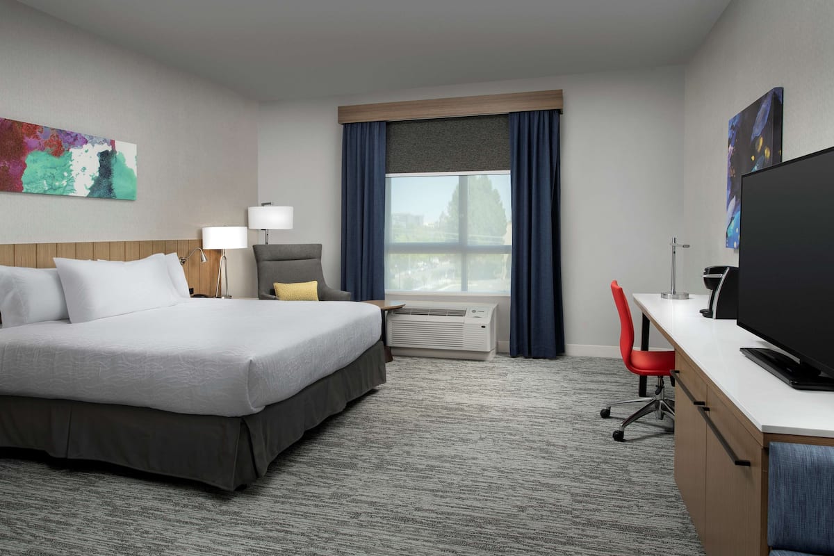 Une chambre d’hôtel avec un lit, un bureau, une télévision et une fenêtre avec des rideaux.