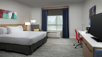 Quarto de hotel com cama, escrivaninha, televisão e janela com cortinas.