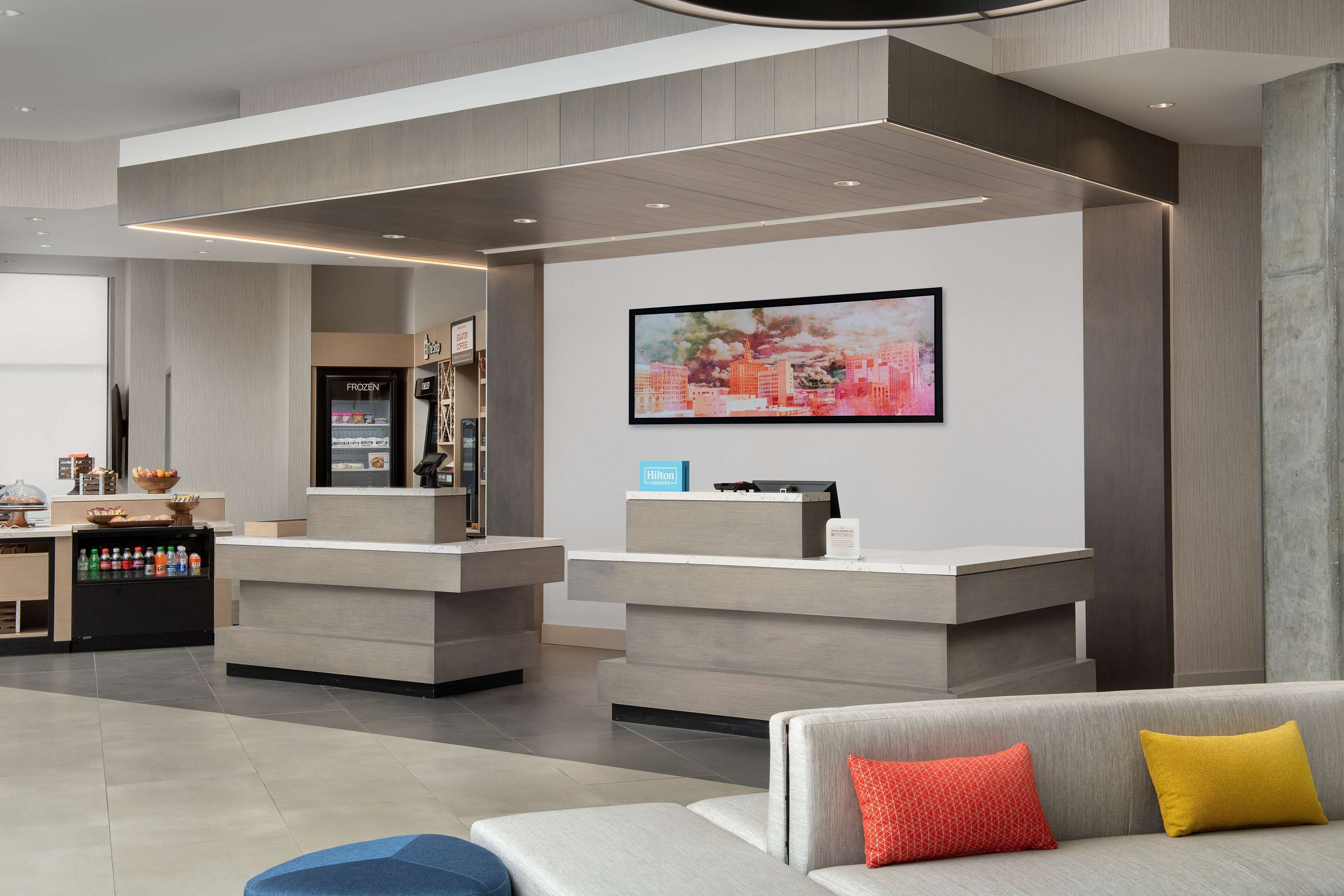 A modern hotel lobby with a reception desk, seating area, and a large cityscape painting.