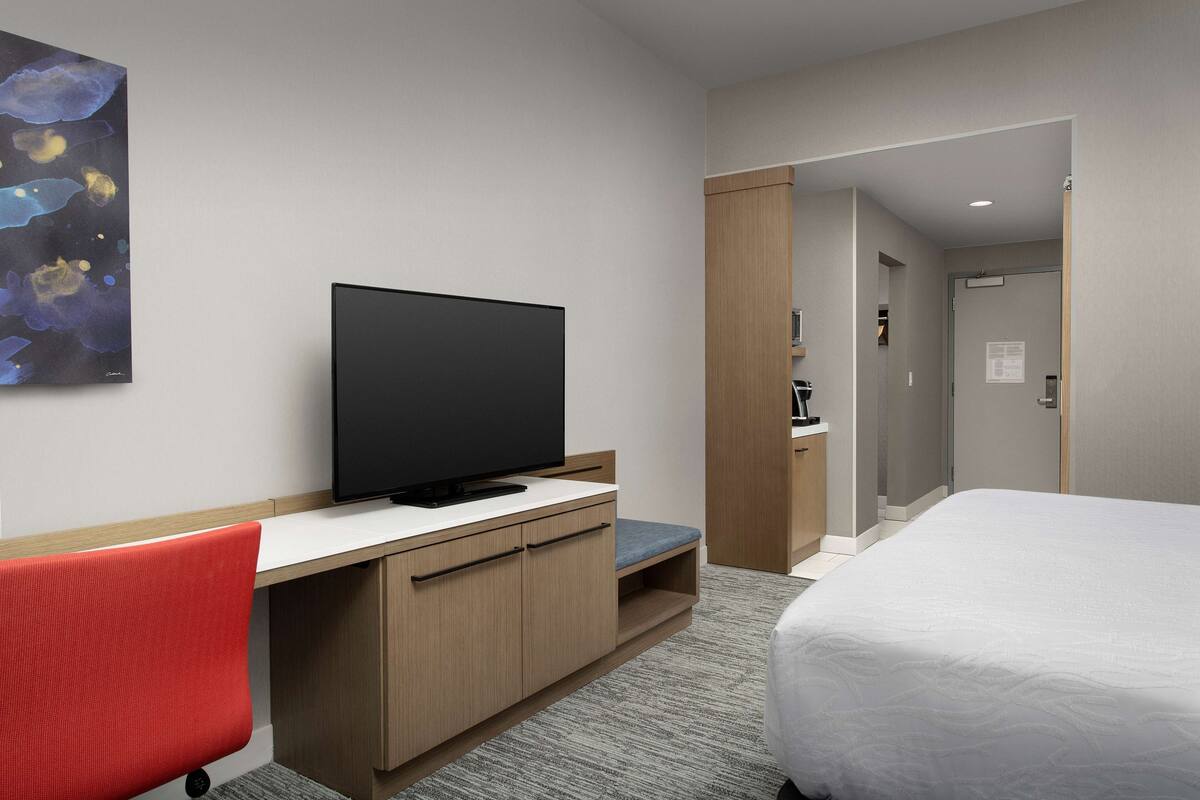 Une chambre d’hôtel équipée d’un téléviseur à écran plat, d’un lit, d’un bureau avec une chaise et d’une porte donnant sur une autre pièce.